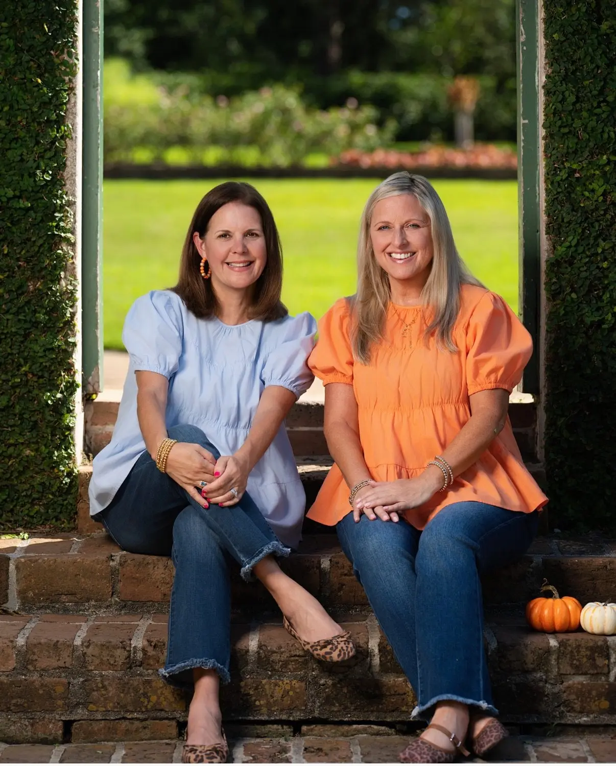 Michelle and Stephanie, founders of the proper porch, seated on brick steps with pumpkins